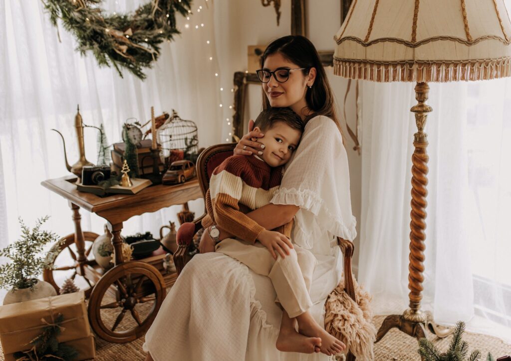 Mother Holding Her Little Son and Sitting in a Room with Christmas Decorations